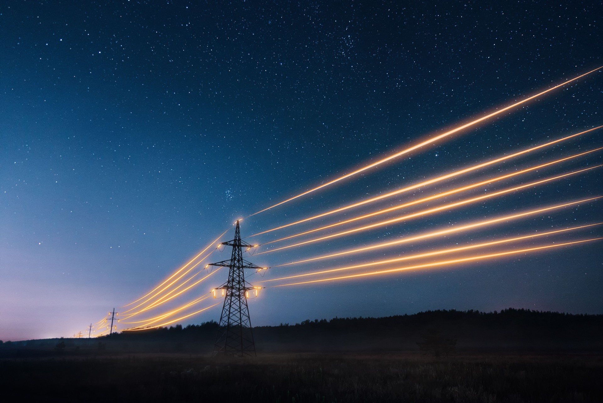 Electricity transmission towers with orange glowing wires against night sky.